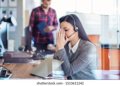 Tired young woman is sitting at the table at work in a call center.