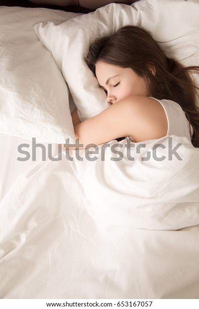 疲れた若い女性は白いシーツを着た柔らかいベッドでよく眠る 寝室で目を閉じて穏やかに休む10代の女性は 甘い夢を楽しみます 完璧な状態 快適な睡眠 トップビュー の写真素材 今すぐ編集
