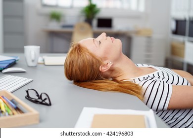 Tired Young Woman Taking A Break At Work Lying Back In Her Chair With Her Head Tilted Back On The Desk And Her Eyes Closed