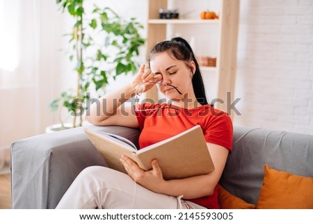 A tired young woman taking off her glasses massages her eyes after reading a book. the feeling of discomfort due to prolonged wearing of glasses, the concept of pain in the eyes. myopia.
