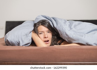 Tired Young Woman Yawning Under A Duvet As She Spends A Lazy Day Relaxing At Home