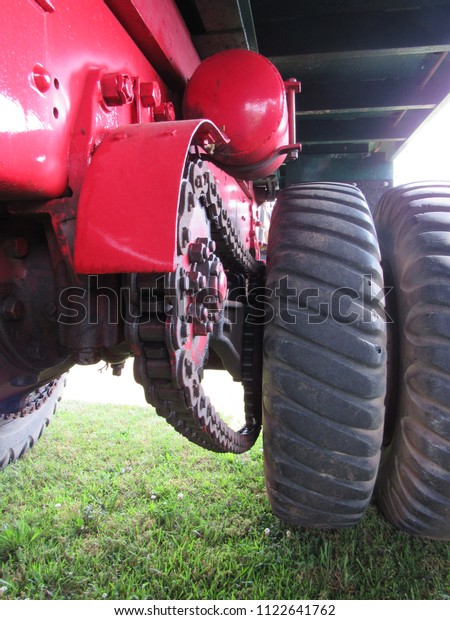 The tires, chains, and underbody of a red truck on\
the grass