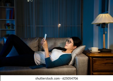 Tiring Female Businesswoman Watching Mobile Phone Relaxing On The Living Room Lying Down On The Sofa With Copyspace Drinking Hot Coffee Resting Moment For Working Over Night.