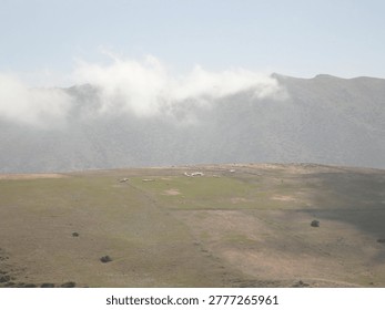 Title: Atmospheric Cloud Inversion over High Mountain Plateaus in Tarom, Iran.

Description: A professional landscape photograph of the rugged Alborz Mountains in Zanjan Province, featuring a thin line of white clouds cascading over the high-altitude ridges. The foreground shows the sun-drenched, arid plateau typical of northern Iran's mountain passes. Ideal for travel editorial, meteorological studies, and Middle Eastern geographic documentation