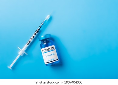 Title: Covid-19, Coronavirus Vaccine Mock Up. Vial Of Blue Coloured Vaccine With A Syringe Isolated On A Blue Background Shot From Above With Copy Space