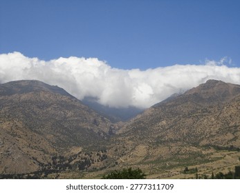 Title: Dramatic Cloud Cascade Over Alborz Mountain Peaks in Tarom, Iran.

Description: A professional landscape photograph showing a thick layer of white clouds spilling over the rugged, sun-baked ridges of the Alborz mountain range. The image captures the unique microclimate of Zanjan Province, where humid northern air meets the dry central plateau. Ideal for travel editorials, meteorological documentation, and Middle Eastern geographic studies.