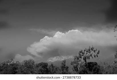 TITLE:
Dramatic storm clouds over mountain landscape in black and white

DESCRIPTION:
Black and white photograph of dramatic storm clouds forming over a mountain landscape with trees in the foreground. High contrast sky creates a powerful and moody atmosphere.
