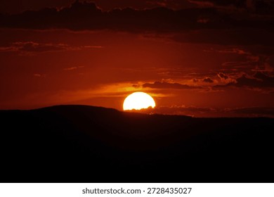 Title : Dramatic Sunset Over Silhouetted Hills and Clouds

Description: Vibrant, dramatic sunset with intense red and orange sky, the sun partially hidden behind clouds, and rolling hills 