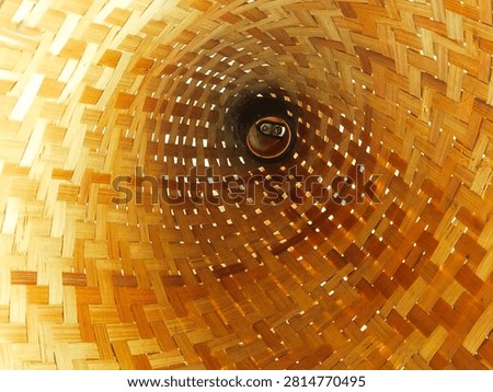 Title (Judul): Abstract perspective inside a woven bamboo cone structure.
Description (Deskripsi): Creative interior view looking through a traditional cone-shaped woven bamboo basket. Showcases a complex interlocking wicker pattern, natural golden-brown textures, and a geometric tunnel perspective with light filtering through the gaps. Ideal for cultural design, abstract architecture, and organic handicraft concepts.