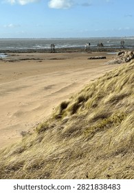 Title: Windswt dune grass overlooking a beach with distant fishing huts

Description: Windswept dune grass frames a view of a sandy beach with distant traditional wooden fishing huts on stilts along the Atlantic coast of Frane