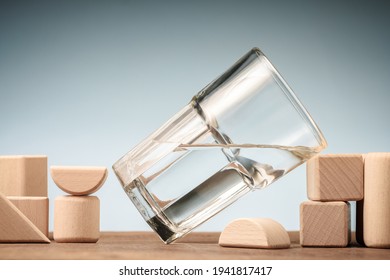 Titled Glass Of Water With Half Full Water Lean On The Wood Block Toy On The Table, Glass Half Full Concept