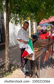 Tlaquepaque, Jalisco, Mexico - September 15 2019: Senior Male Marimba Player Outdoors Under A Tree. Mexican Flag