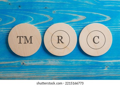 TM, R and C signs each written on its own wooden cut circle placed over blue wooden background.