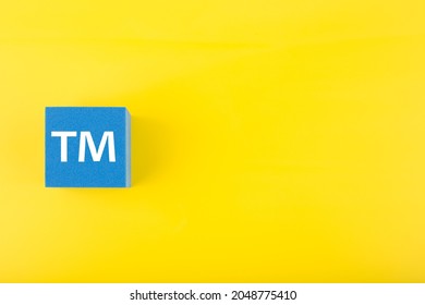 TM trademark sign on blue toy cube on yellow background with copy space. Concept of intellectual property registration and protection