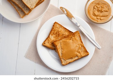 Toast bread and Homemade peanut butter.Spreading peanut butter on slice whole wheat bread in white plate.Top view - Powered by Shutterstock