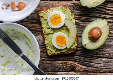 Toast With Mashed Avocado And Eggs On Messy Rustic Wooden Table From Above