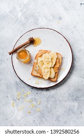 Toast With Peanut Butter, Banana Slices, Honey And Almond Flakes On An Old Gray Concrete Background. Top View.