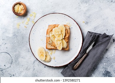 Toast With Peanut Butter, Banana Slices, Honey And Almond Flakes On Old Gray Concrete Background. Top View.