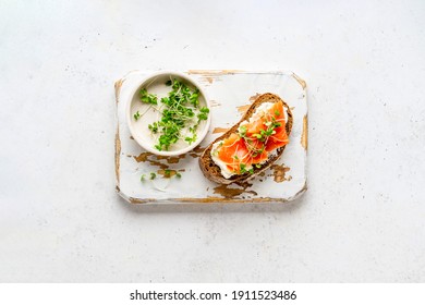Toast with ricotta (cream cheese), smoked salmon and micro greens served on wooden rustic board. Health care, super food concept. White Stone background. Top view.
