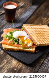 
Toast with salmon, poached egg and guacamole. Liquid yolk. Breakfast on a wooden table, served with a kettle, shot, spices and herbs. Restaurant, cafe, bar menu. Сlose up.