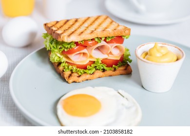 Toast sandwich with gouda cheese and turkey ham filled with tomato and lettuce on a bright background with ingredients in blurry background. Served with coffee and orange juice and eggs