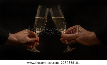 Toast with sparkling wine or champagne glasses on dark black night background - Young woman und man holding glass in the hand