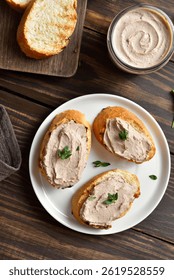 Toasted bread with chicken liver pate on white plate on wooden table. Top view, flat lay