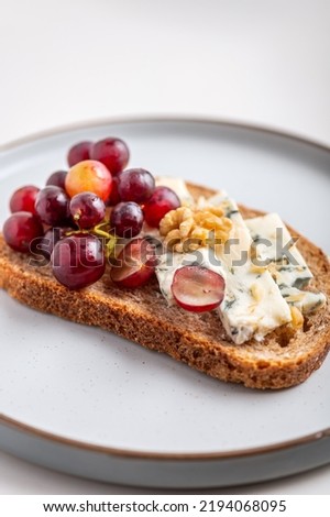 Toasted bread with mild creamy blue cheese, grapes and walnuts on grey plate