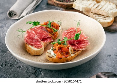 toasted bread with salami and tomatoes and herbs on a plate on the kitchen table. Open sandwiches with Italian salami