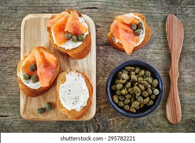 toasted bread slices with cream cheese and smoked salmon on wooden cutting board, top view