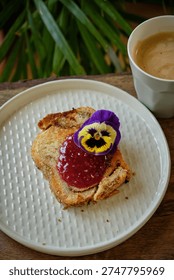 Toasted brioche slice with raspberry jam and edible pansy flower.