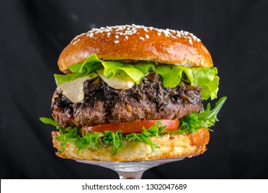 Toasted brown hamburger with mushrooms champignons, cheese, tomato sauce, a piece of fried bacon, juicy steak pork or beef, and tomato wooden chopping board, Isolated on black background - Powered by Shutterstock