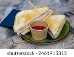 Toasted ham and cheese sandwich in the plate served with tomato ketchup sauce on the side, The tosti in Netherlands or croque-monsieur is a hot sandwich made with ham and cheese.