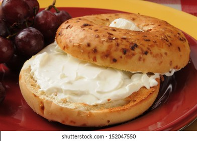 A Toasted Onion Bagel With Cream Cheese And Grapes