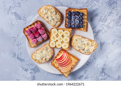 Toasted sandwich bread with peanut butter, banana, frozen berries raspberries, blueberries. Served on concrete background. Healthy, balanced traditional breakfast. Vegan sweet dessert, top view