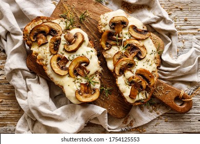 Toasted sandwich from traditional sourdough bread with cheese and brown mushrooms seasoned with rosemary herb on a wooden board, top view - Shutterstock ID 1754125553