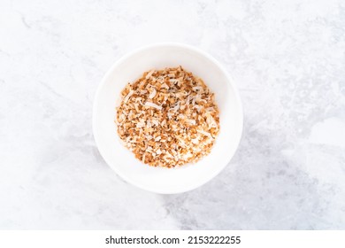 Toasted shredded coconut flakes in a white ceramic bowl.