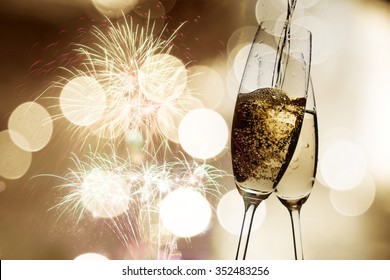 Toasting with champagne glasses against holiday lights, fireworks and clock at midnight