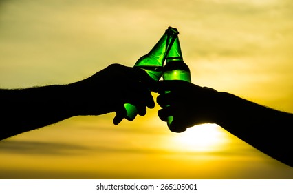 toasting with green bottle beers against summer sky / sun