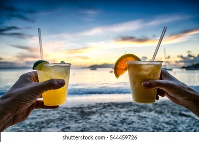 Toasting with tropical drinks at sunset with island beach background; focus on drinks