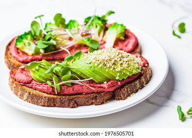 Toasts with beetroot hummus, avocado and broccoli on white plate. Vegan food concept.