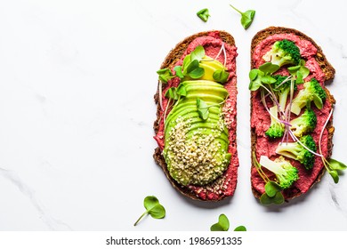 Toasts with beetroot hummus, avocado and broccoli, white marble background, top view. Vegan food concept.