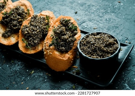 Toasts with black caviar on a stone plate, caviar in a bowl. On a black stone background. Rustic style.