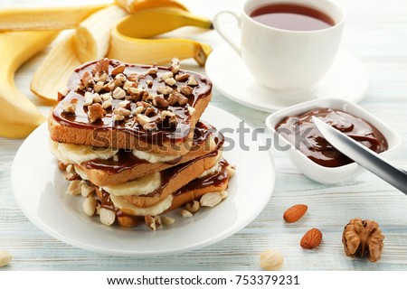 Toasts bread with bananas, walnuts and chocolate on white wooden table
