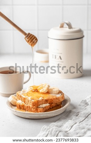 Toasts with butter and banana slices with honey dripping from honey spoon on light kitchen background. Homemade breakfast sandwich. Healthy vegan food. Vertical