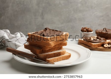 Toasts with chocolate paste, hazelnuts and knife on white marble table, closeup