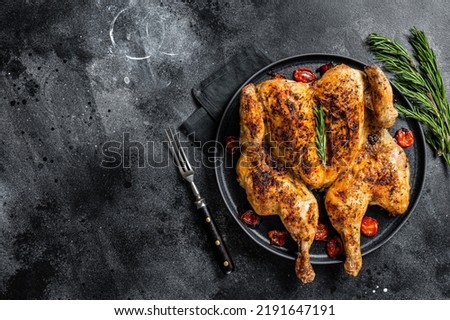 Tobacco whole chicken on plate with herbs and tomato. Black background. Top view. Copy space
