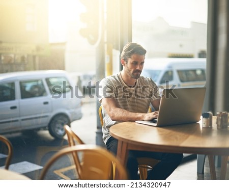 Todays tech allows you to work anywhere. Shot of a young man working on his laptop in a coffee shop.