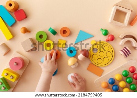 Toddler activity for motor and sensory development. Baby hands with colorful wooden toys on table from above.