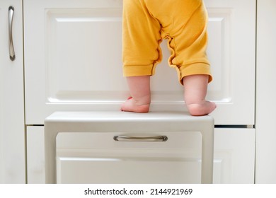 Toddler Baby Boy Climbed With His Feet On A High Chair To Climb On The Kitchen Cabinet. Child Safety Issues In The Home Room, Little Kid